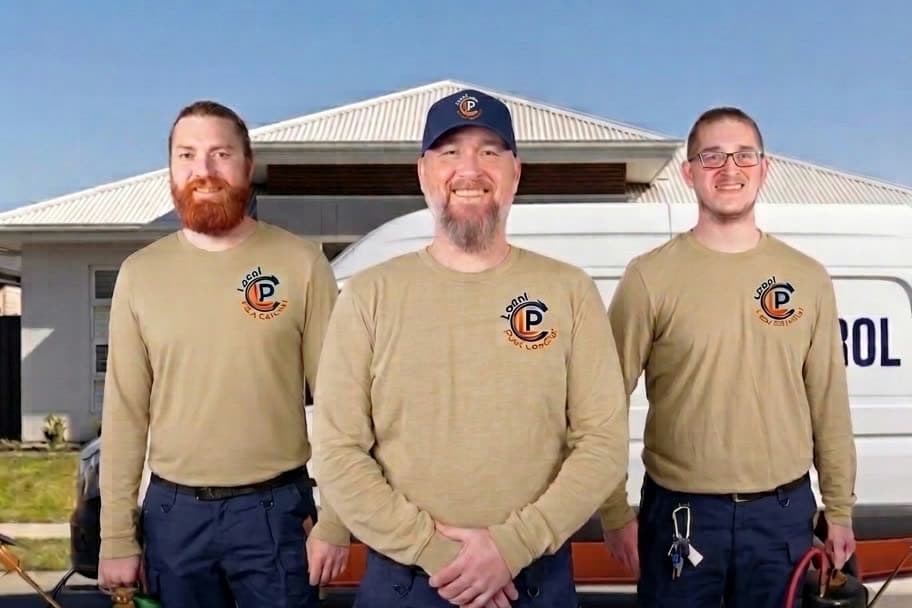 Local Pest Control team β three smiling licensed and insured technicians in khaki uniform shirts in front of the company van